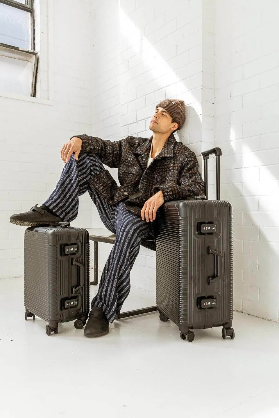 Model in stylish outfit posing with travel luggage in a bright, modern space.